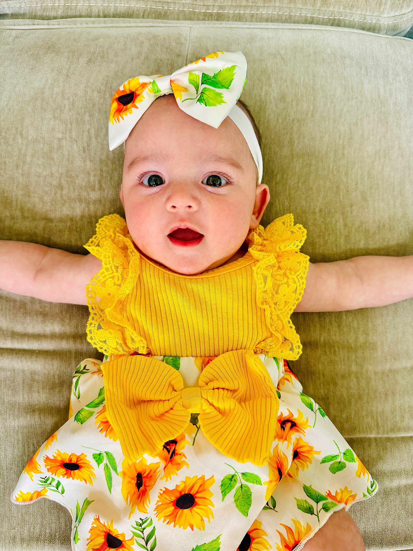 Arya Rosie joined the competition — help win amazing prizes! baby, infant, child, sunflower, headband, dress, yellow, cute, smile, face, arms, clothing, pattern, sitting, couch, indoors, happy, portrait, person, young