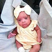 Iyana is registered to the contest to win money with this photo: baby, infant, child, portrait, sitting, yellow_outfit, bow, headband, white_blanket, sock, crossed_legs, face, eyes, looking_at_camera, indoor, soft_fabric, seated, baby_clothing, candid, cute