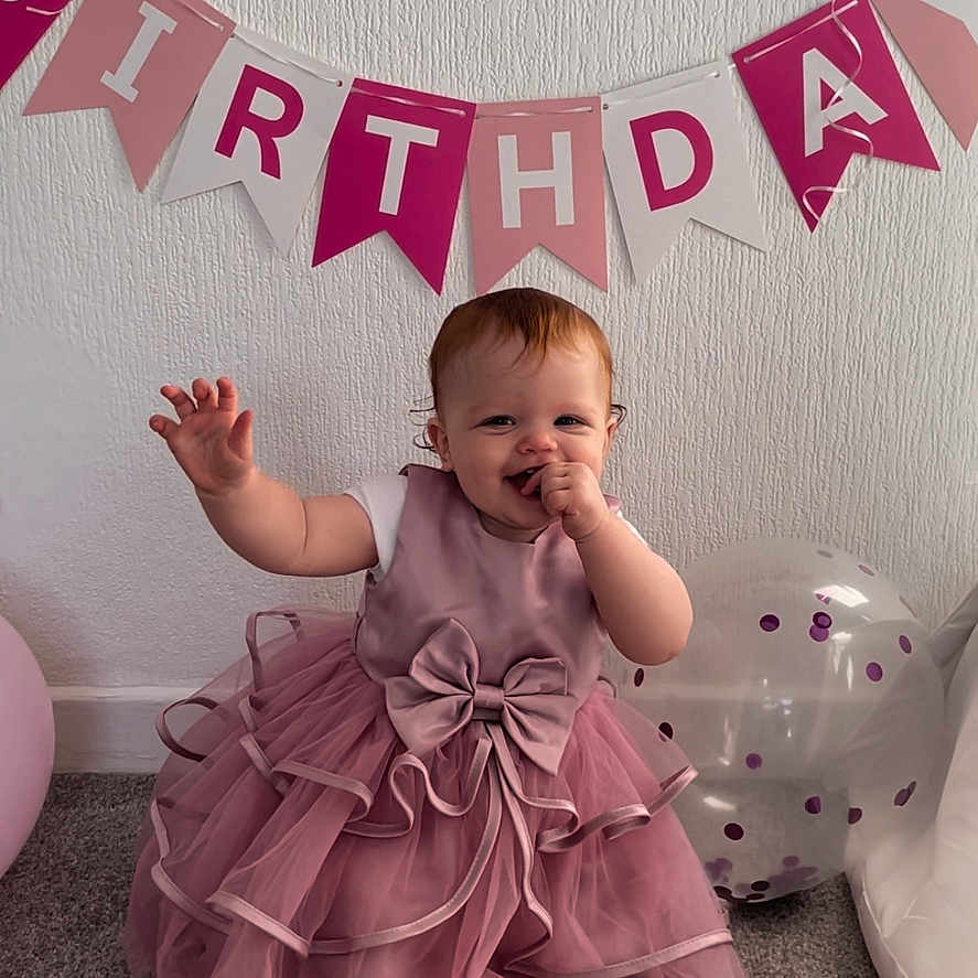 Valentina is registered to the contest to win money with this photo: baby, balloon, banner, birthday, bow, carpet, celebration, child, cute, decorations, dress, festive, happy, indoor, party, person, pink_dress, sitting, smiling, tulle