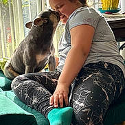 King Peanut joined the competition — help win amazing prizes! dog, person, child, kiss, affection, indoors, sitting, chair, window, sunlight, pet, companion, portrait, 家庭, clothing, leggings, spiderweb_pattern, teal, furniture, cuddling