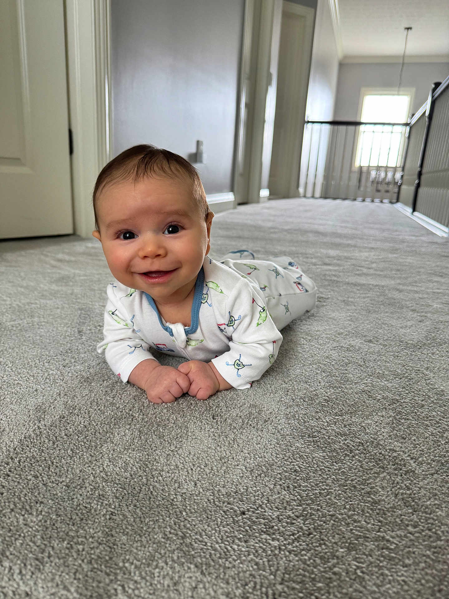 Archie is registered to the contest to win money with this photo: baby, infant, carpet, smiling, indoor, hallway, floor, clothing, person, cute, child, home, natural_light, window, door, white_wall, happy, lying_down, portrait, young_child