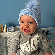 Kaven is registered to the contest to win money with this photo: baby, child, smile, hat, pom_pom, blue_hat, gray_outfit, crib, bedding, stars, indoor, happy, teeth, cute, infant, clothing, person, portrait, baby_toy, soft_toys
