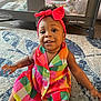 Autumn J is registered to the contest to win money with this photo: baby, child, girl, smiling, headband, bow, colorful_dress, plaid, carpet, indoor, playpen, floor, sitting, happy, cute, person, portrait, young_child, infant, home
