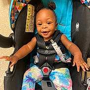 Autumn J is registered to the contest to win money with this photo: baby, child, car_seat, colorful, smiling, happy, infant, pigtails, hair_buns, toddler, clothing, patterned_pants, straps, safety_harness, indoor, floor, cute, reaching_out, person, seat