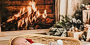 Bjorn is registered to the contest to win money with this photo: baby, basket, fireplace, fire, cozy, holiday, decorations, gift, wrapped_gift, plush_rug, smiling, infant, warm, indoors, wood, wicker, blanket, clothing, socks, festive