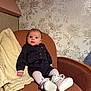 baby, infant, armchair, blanket, clothing, footwear, tights, person, portrait, indoor, furniture, patterned_wallpaper, cute, sitting, looking, cozy, decor, small_shoes, black_outfit, white_tights