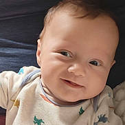 Colten joined the competition — help win amazing prizes! baby, infant, smiling, face, eyes, onesie, clothing, dinosaur_print, cute, cheeky, lying_down, child, skin, head, hair, expression, portrait, indoors, soft_light, happy