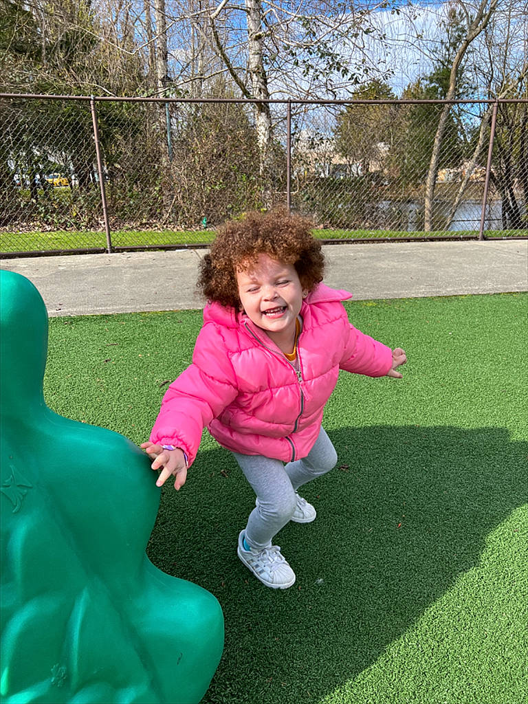 Guinda is registered to the contest to win money with this photo: city, fun, grass, happy, joy, lawn, leisure, magenta, outdoor_play_equipment, people_in_nature, person, pink, plant, play, playground, recreation, sitting, sky, smile, toddler