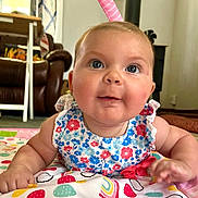 Ruth joined the competition — help win amazing prizes! baby, child, infant, blue_eyes, floral_dress, play_mat, indoor, living_room, carpet, furniture, curtains, colorful, cute, portrait, smiling, person, skin, hand, face, cheeks