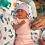 Riley is registered to the contest to win money with this photo: newborn, baby, hospital, incubator, medical_tube, pink_clothing, striped_hat, hand, holding_hand, blanket, footprint_pattern, infant, patient, healthcare, bed, person, cute, small, lying_down, nursery