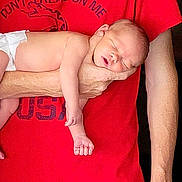 Leland is registered to the contest to win money with this photo: baby, newborn, sleeping, diaper, arm, person, red_shirt, hand, skin, peaceful, infant, closeup, portrait, indoor, human, child, resting, casual, comfort, toddler