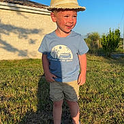 Rafaël a rejoint le concours — aidez-le/la à gagner de superbes lots ! child, boy, outdoor, grass, blue_sky, straw_hat, tshirt, shorts, sandals, smiling, sunlight, shadow, stone_wall, nature, summer, vacation, happy, person, casual_clothing, daytime