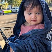 Avery is registered to the contest to win money with this photo: toddler, child, shopping_cart, hooded_jacket, blue_clothing, outdoor, daylight, trees, face, eyes, curious, street, parked_cars, clothing, person, portrait, cute, infant, baby, smiling