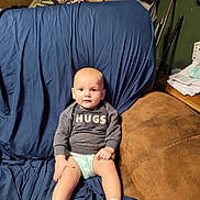 Nicco joined the competition — help win amazing prizes! baby, child, sitting, couch, socks, diaper, sweater, indoor, furniture, expression, face, person, living_room, blanket, blue_cover, brown_couch, curious, young_child, casual, home
