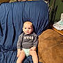 baby, child, sitting, couch, socks, diaper, sweater, indoor, furniture, expression, face, person, living_room, blanket, blue_cover, brown_couch, curious, young_child, casual, home