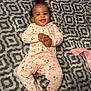 baby, infant, child, smiling, onesie, floral_pattern, blanket, cozy, lying_down, happy, cute, indoors, portrait, hands_clasped, footed_pajamas, patterned_blanket, soft_texture, baby_girl, relaxed, sleepwear