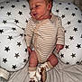 Maddox is registered to the contest to win money with this photo: newborn, baby, infant, onesie, striped_clothing, socks, lion_socks, pillow, star_pattern, blanket, pacifier, baby_bottle, sleepy, lying_down, cute, soft_toy, indoor, child, resting, peaceful