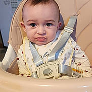 Luna'Rae is registered to the contest to win money with this photo: baby, high_chair, bib, straps, indoor, kitchen, fridge, face, expression, child, clothing, seat, person, young, cute, pout, sitting, infant, home, portrait