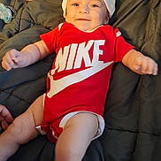 Luna'Rae is registered to the contest to win money with this photo: baby, infant, smiling, red_clothing, nike_logo, baby_bottle, pacifier, blanket, lying_down, hat, sock, cute, happy, indoor, child, person, portrait, soft_lighting, comfort, playful