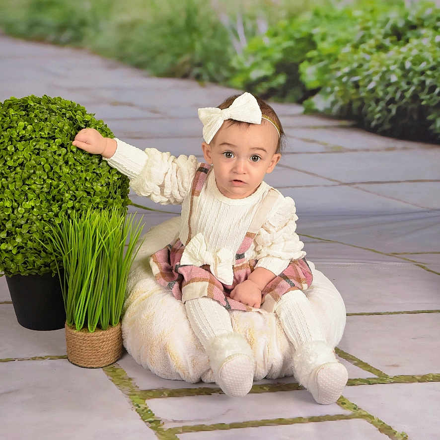 Luna'Rae is registered to the contest to win money with this photo: baby, bow, bush, child, cushion, dress, floor_tiles, girl, grass, hand, headband, infant, plush, portrait, pose, potted_plant, sitting, socks, studio_backdrop, surprised_expression