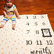 Luna'Rae joined the competition — help win amazing prizes! baby, celebration, child, clothing, cute, floor, headwear, indoor, infant, milestone_blanket, months, numbers, person, pink_bow, portrait, sitting, smile, striped_clothing, wooden_floor, young_child