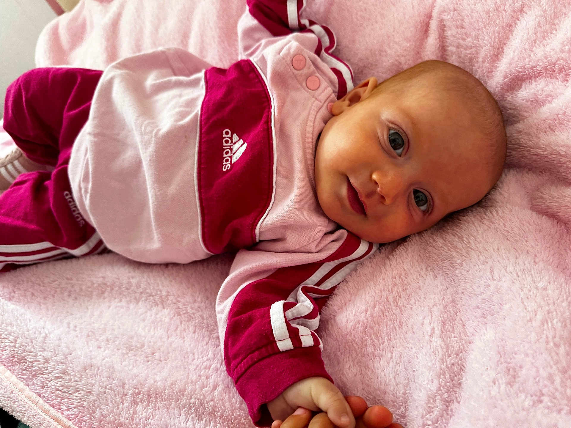 Maïvy participe au concours pour gagner de l'argent avec cette photo : baby, infant, child, pink_blanket, adidas_clothing, sporty_outfit, lying_down, cute, portrait, face, hand, soft_texture, relaxed, indoor, closeup, smiling, young_child, casual_wear, comfortable, resting