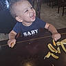 baby, child, toddler, smiling, laughing, face, portrait, restaurant, dining_room, table, french_fries, food, eating, high_chair, chair, blue_shirt, short_hair, indoor, happy, casual_photo
