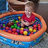 Micaiah is registered to the contest to win money with this photo: toddler, child, ball_pit, smiling, laughing, indoor, playtime, colorful_balls, plastic_pool, football, adult, hand, red_shirt, shorts, cartoon, toy, carpet, living_room, portrait, happy