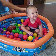 Micaiah joined the competition — help win amazing prizes! baby, toddler, child, smiling, happy, ball_pit, playroom, colorful_balls, inflatable_pool, toy, football, indoor, sitting, playing, portrait, face, adult, carpet, home, fun