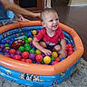 baby, toddler, child, smiling, happy, ball_pit, playroom, colorful_balls, inflatable_pool, toy, football, indoor, sitting, playing, portrait, face, adult, carpet, home, fun
