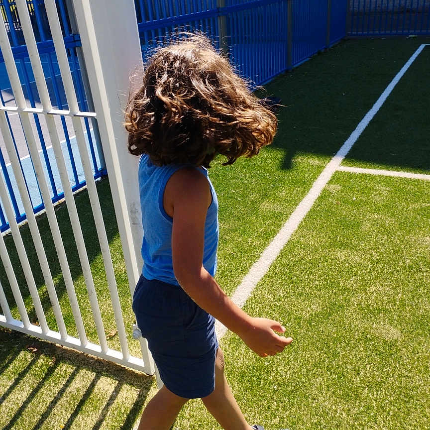 Zwak joined the competition — help win amazing prizes! athletic, blue_tank_top, casual_clothing, child, curly_hair, daylight, green_grass, movement, outdoor, person, playground, shadow, shorts, side_view, sneakers, sports_field, sunlight, walking, white_fence, young