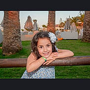 Eva joined the competition — help win amazing prizes! child, girl, smile, flower, hair_accessory, wooden_rail, grass, palm_tree, outdoor, daylight, happy, portrait, nature, casual_clothing, greenery, sunlight, park, relaxation, vacation, leisure