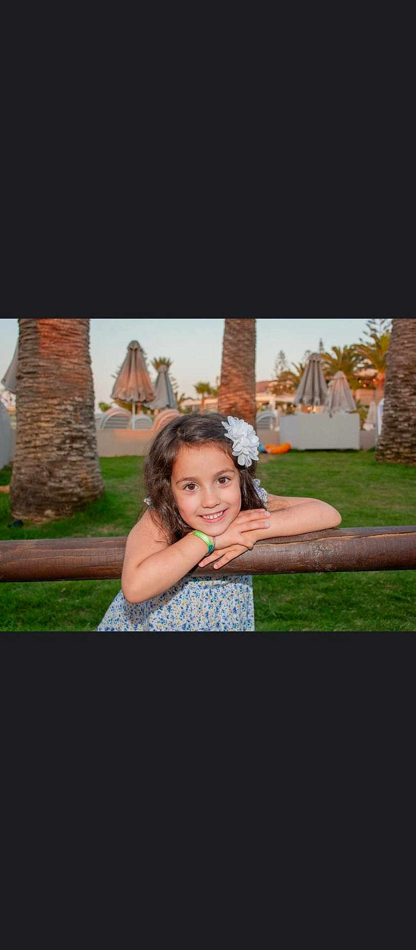 Eva joined the competition — help win amazing prizes! child, girl, smile, flower, hair_accessory, wooden_rail, grass, palm_tree, outdoor, daylight, happy, portrait, nature, casual_clothing, greenery, sunlight, park, relaxation, vacation, leisure
