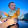 Jaxtyn joined the competition — help win amazing prizes! baby, infant, child, teether, bib, holding, adult_hand, tattoo, car, hood, reflection, blue_sky, outdoor, portrait, bokeh, cute, clothing, eyes, cheek, sitting