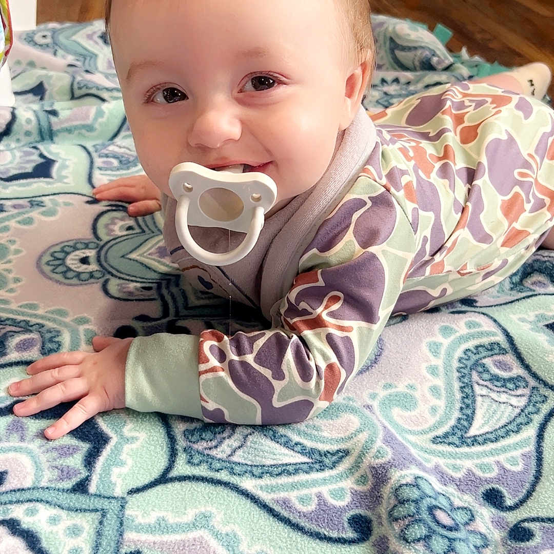 Jaxtyn joined the competition — help win amazing prizes! baby, blanket, closeup, crawling, drool, eyes, face, hair, hands, indoor, lying_down, onesie, pacifier, patterned_clothing, playmat, portrait, rug, smiling, toy, wooden_floor