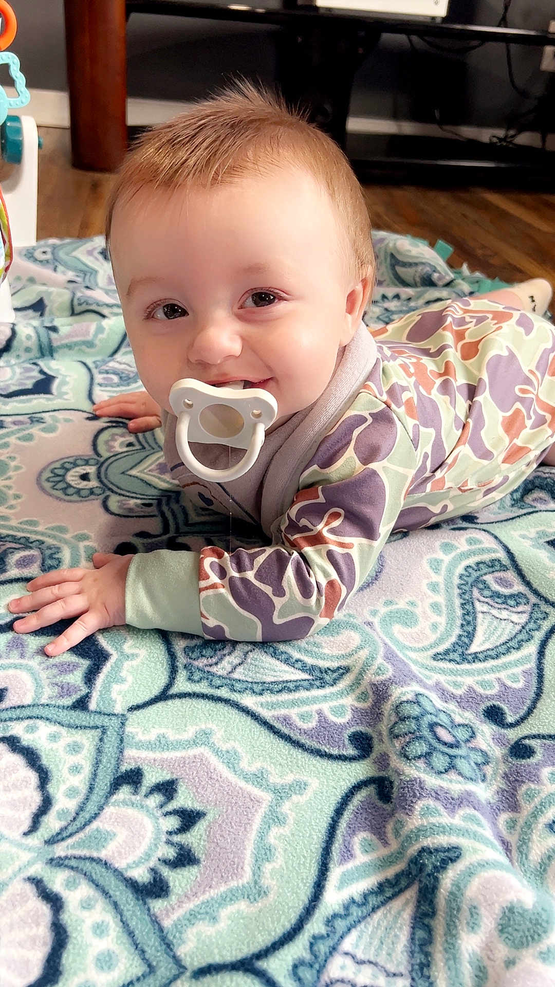 Jaxtyn joined the competition — help win amazing prizes! baby, pacifier, blanket, smiling, lying_down, onesie, patterned_clothing, hands, eyes, hair, face, drool, wooden_floor, rug, playmat, toy, indoor, portrait, closeup, crawling