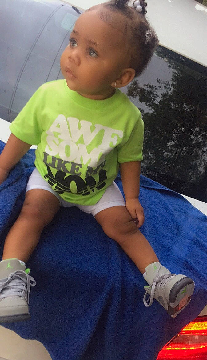 Aniyah Dior Marshall is registered to the contest to win money with this photo: baby, baby_toddler_clothing, black, child, electric_blue, eye, fun, grass, happy, head, human_leg, knee, leisure, person, shorts, sitting, sleeve, sneakers, t_shirt, thigh