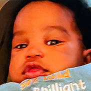 Karter is registered to the contest to win money with this photo: baby, infant, face, closeup, child, black_hair, expressionless, clothing, text_on_clothing, portrait, young_child, cute, skin, head, indoors, person, soft_focus, calm, relaxed, baby_girl