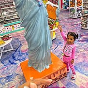 Grace joined the competition — help win amazing prizes! child, girl, pink_pajamas, smiling, statue, chocolate, candy_store, colorful_floor, toy_shelves, indoor, happy, playful, retail, snacks, lollipop, statue_of_liberty_style, floor_pattern, store_display, person, excited