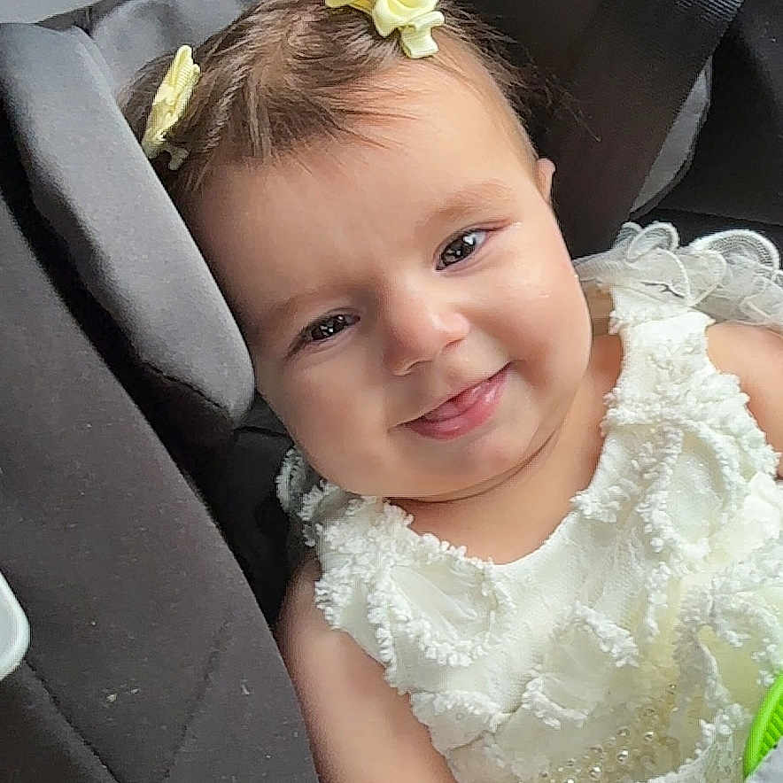 Pelin joined the competition — help win amazing prizes! baby, car_interior, car_seat, child, closeup, cute, dress, hair_bow, happy, holding, indoor, infant, portrait, safety_label, seat, seatbelt, smile, toy, white_dress, young_child