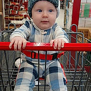 Alistair joined the competition — help win amazing prizes! baby, child, shopping_cart, hat, plaid_clothing, blue_eyes, indoor, store, aisle, red_handlebar, socks, seatbelt, clothing, person, cute, infant, retail, shopping, cart, curious