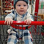 baby, child, shopping_cart, hat, plaid_clothing, blue_eyes, indoor, store, aisle, red_handlebar, socks, seatbelt, clothing, person, cute, infant, retail, shopping, cart, curious
