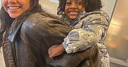 Harlem is registered to the contest to win money with this photo: child, children, smiling, piggyback, leather_jacket, curly_hair, braces, indoor, happy, person, coats, jackets, frosted_glass, background, portrait, playful, sibling, young, casual, fun