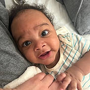 Carmello joined the competition — help win amazing prizes! baby, infant, child, hand, bed, blanket, pacifier, curly_hair, striped_clothing, smile, close_up, skin, cute, person, fingers, lying_down, soft_toys, comfort, indoors, family