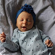 Harper is registered to the contest to win money with this photo: baby, infant, smile, blue_headband, flower, patterned_clothing, blanket, lying_down, cozy, cute, happy, child, newborn, soft_lighting, portrait, baby_clothes, hands, face, headwear, comfortable