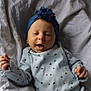 baby, infant, smile, blue_headband, flower, patterned_clothing, blanket, lying_down, cozy, cute, happy, child, newborn, soft_lighting, portrait, baby_clothes, hands, face, headwear, comfortable