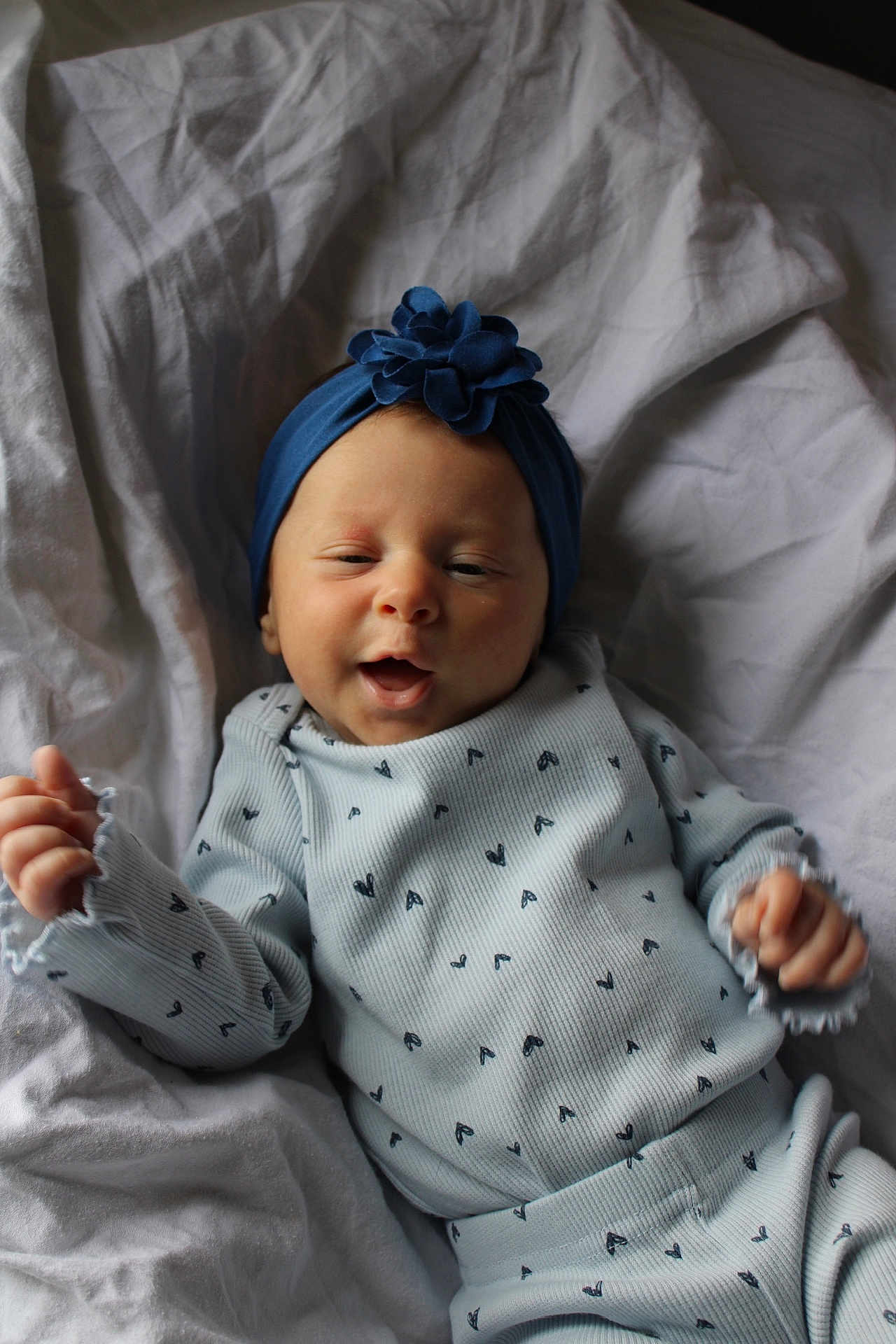Harper is registered to the contest to win money with this photo: baby, infant, smile, blue_headband, flower, patterned_clothing, blanket, lying_down, cozy, cute, happy, child, newborn, soft_lighting, portrait, baby_clothes, hands, face, headwear, comfortable