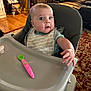 baby, high_chair, spoon, bib, indoor, carpet, furniture, living_room, toy, child, person, curious, seat, expression, wood_floor, plush_toy, couch, table, household, reaching_hand