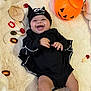 4_months, baby, bat_costume, black_outfit, candy, celebration, child, cute, fluffy_blanket, halloween_costume, happy, hat, holiday, indoors, infant, lying_down, person, pumpkin_bucket, smiling, wooden_sign