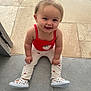 baby, child, smiling, sitting, floor, red_top, white_pants, heart_pattern, strawberry_design, shoes, indoor, happy, cute, person, portrait, toddler, young_child, face, human, casual_clothing